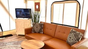 A modern living room with a leather sofa, a small round table, and a patterned rug. - The Laredo, Luxury Safari Tent (Cadiz)