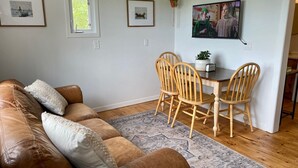 Een woonkamer met een bruine leren bank, een houten eettafel met vier stoelen en een kamerkleed met een patroon.