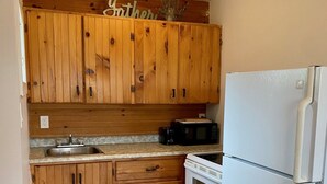 Een kleine keuken met houten kastjes, een witte koelkast, een magnetron en een fornuis.