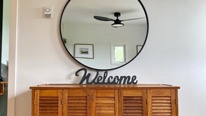 Een houten kast met een ronde spiegel en een bordje met de tekst 'Welcome' erboven.