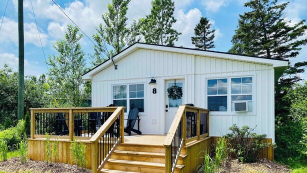 Een klein, gelijkvloers huis met een veranda en houten trap naar de voordeur.