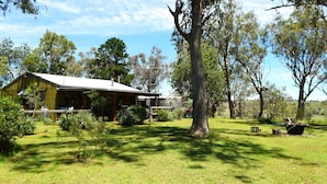 A rustic wooden house with a porch, surrounded by a well-maintained lawn and trees. - Little House in the Nursery (Wallabadah)