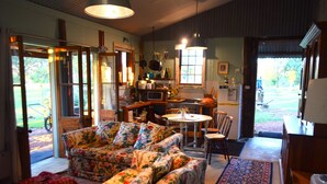 A cozy living room with a floral sofa, a dining table, and a kitchen area with a refrigerator and microwave. - Little House in the Nursery (Wallabadah)