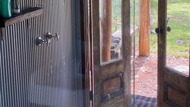 A room with a glass door leading to an outdoor area, a metal shelf with toiletries, and a wooden door with a doormat. - Little House in the Nursery (Wallabadah)