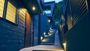 Una escalera estrecha y bien iluminada que sube a un segundo piso, flanqueada por revestimiento de madera y una pared de concreto.