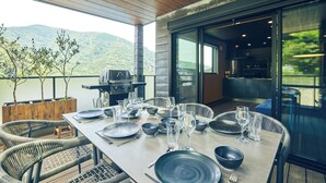 Comedor con mesa dispuesta para seis personas, rodeado de sillas de mimbre, con vistas a un paisaje montañoso.
