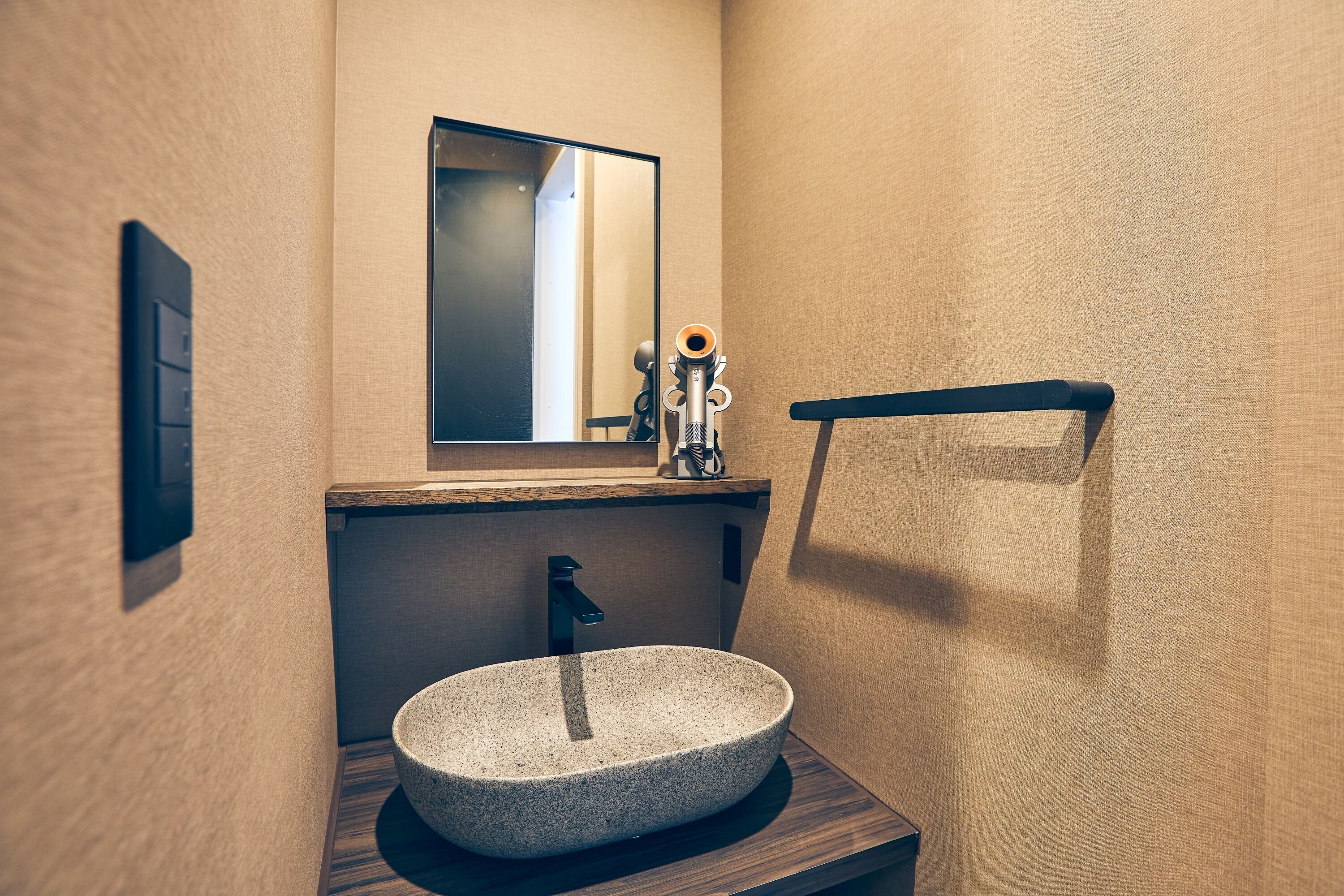 Un baño con un lavabo de piedra, un espejo, un perchero para toallas y un dispensador de jabón.