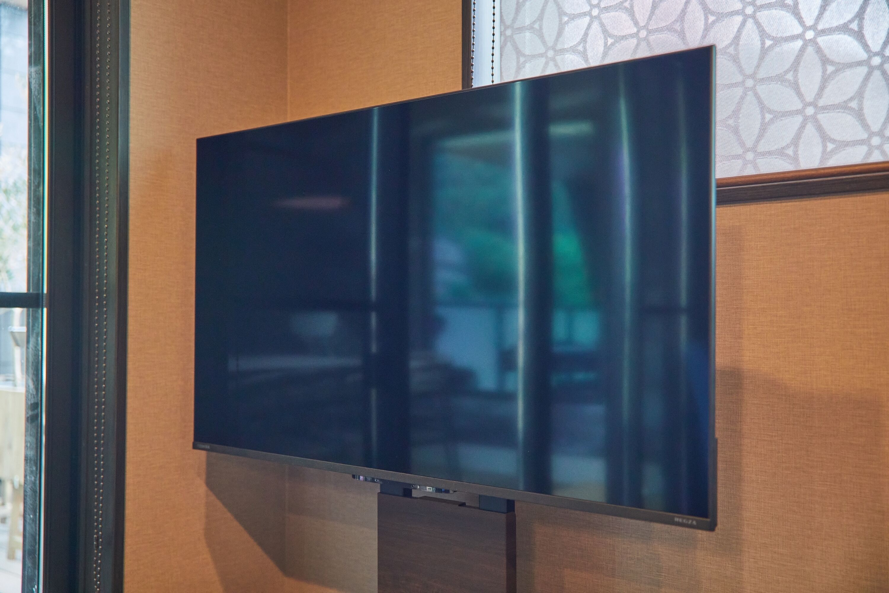 A flat-screen TV mounted on a wall with a wooden panel and a decorative pattern in the background.
