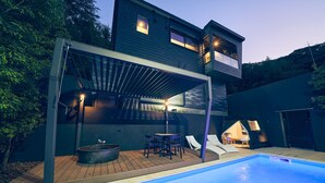 Un área de piscina moderna al aire libre, con zona de estar cubierta y jacuzzi.