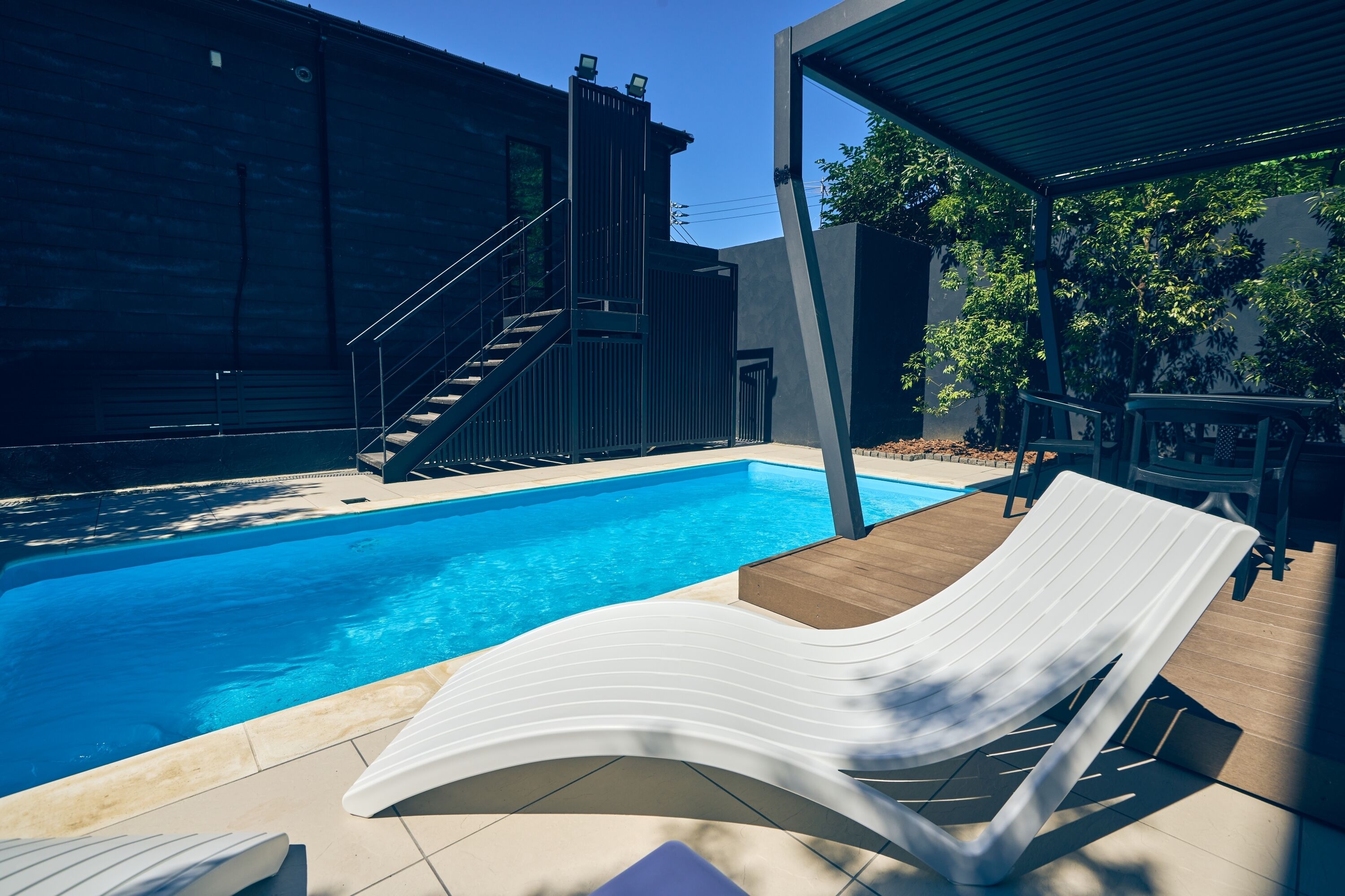 A swimming pool with a white lounge chair, a staircase, and a covered patio area.