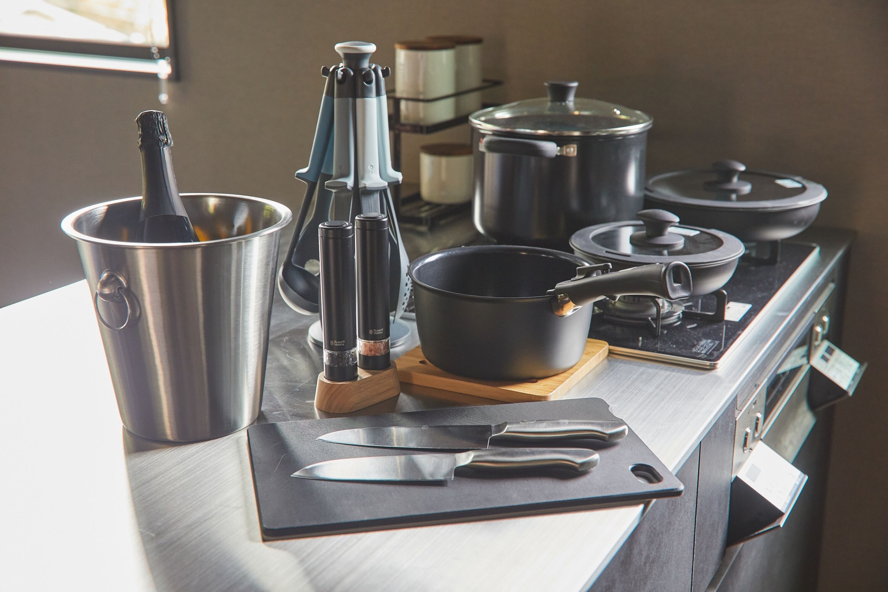 A kitchen counter with a bottle of champagne, a coffee press, a knife, and pots on a stove.
