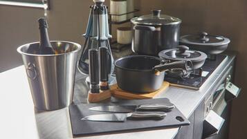 A kitchen counter with a bottle of champagne, a coffee press, a knife, and pots on a stove.