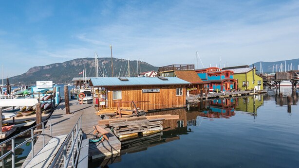 A marina with wooden buildings, boats, and a calm water body reflecting the structures.