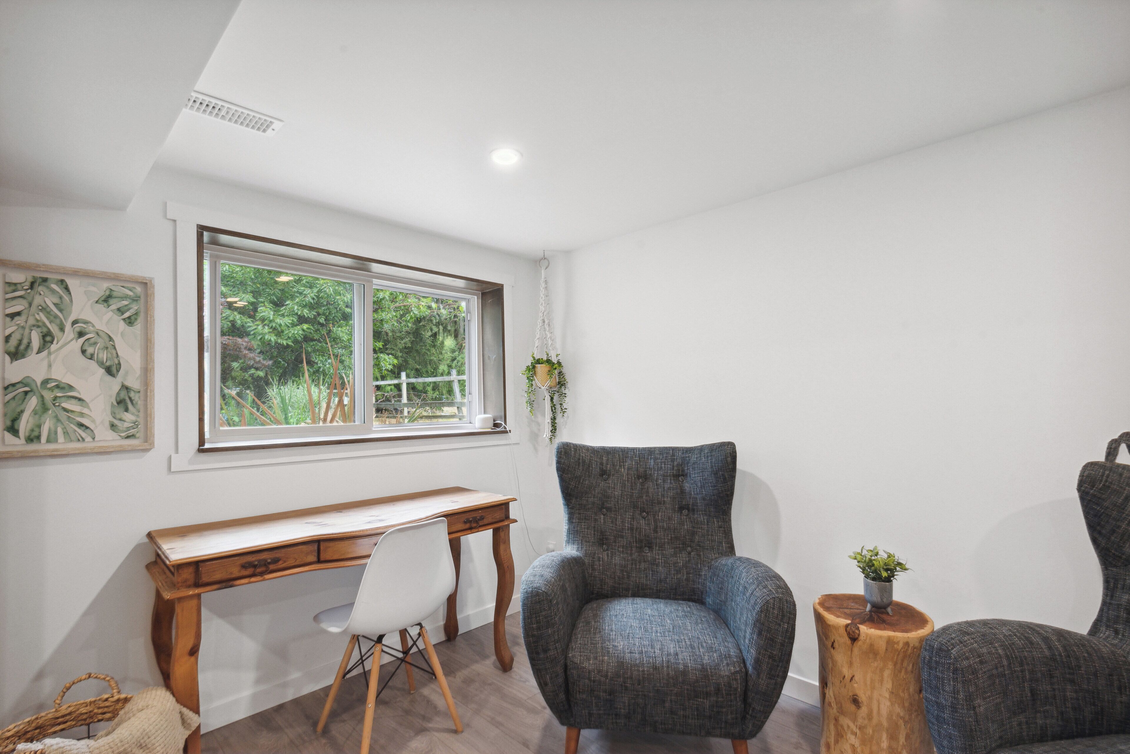 Una habitación con un escritorio de madera, un sillón gris y un taburete de madera con una planta.