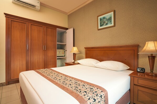 Une chambre d’hôtel avec un grand lit, une armoire en bois, une table de chevet avec une lampe et un tableau au mur.