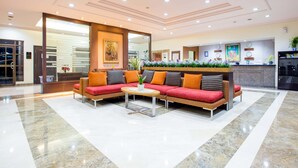 A modern lobby with a sectional sofa, a coffee table, and a reception desk. - Asuka Hotel MM2100 Industrial Town (Cikarang)