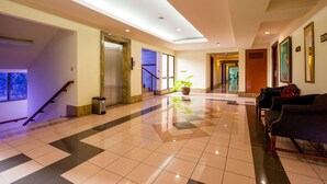 A hotel lobby with a tiled floor, a staircase, a reception desk, and a seating area. - Asuka Hotel MM2100 Industrial Town (Cikarang)