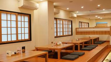 A row of wooden tables with cushioned seats, air conditioning units on the walls, and a view of the outside through large windows.