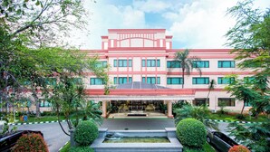 A large building with a red and white facade, surrounded by well-maintained gardens and a central water feature. - Asuka Hotel MM2100 Industrial Town (Cikarang)