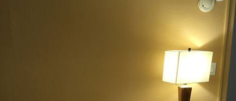 A hotel room with a bed, pillows, a nightstand with a lamp, and a trash bin.