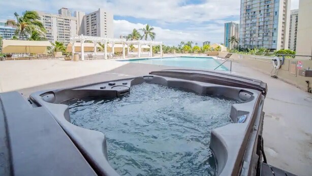 A hot tub with a view of a pool and high-rise buildings in the background. - A Cozy and Romantic Studio at Heart of Waikiki (Honolulu)