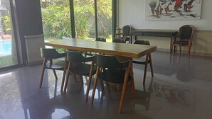 A spacious room with a large window, a wooden table, and several chairs. - Villa Mertanadi 18 (Seminyak)