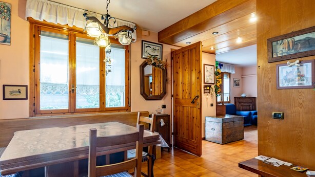 Un comedor con una mesa y sillas de madera, una araña y vistas a través de amplios ventanales.