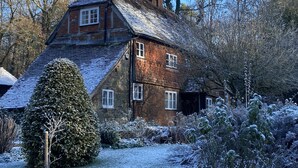 Una casa de ladrillo tradicional con un techo a dos aguas pronunciado, rodeada de árboles cubiertos de nieve y un jardín bien cuidado.