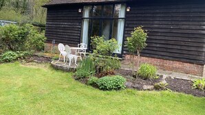 A wooden house with a brick foundation, a chimney, and a garden with a lawn and various plants. - Beautiful one Bed Barn in national park 1 hr from London with small pool (Petworth)