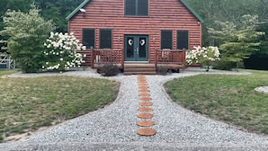 Uma cabana de toras com varanda, duas janelas e uma porta decorada com guirlandas.