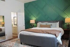 Una cama bien tendida con cabecera gris, un tapete estampado y una pared de acento verde.
