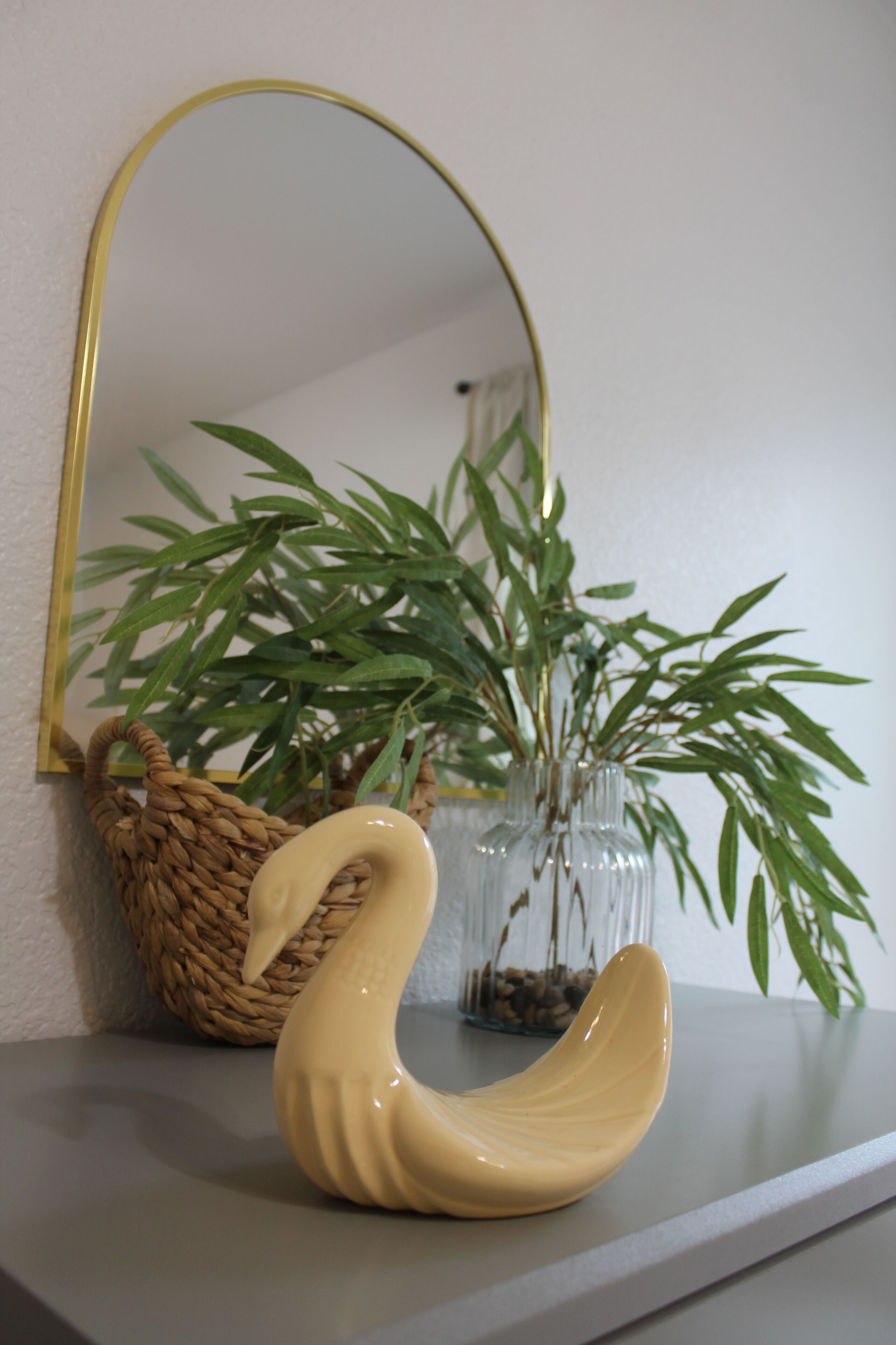 A swan-shaped ceramic object on a shelf, a woven basket, and a potted plant with green leaves.