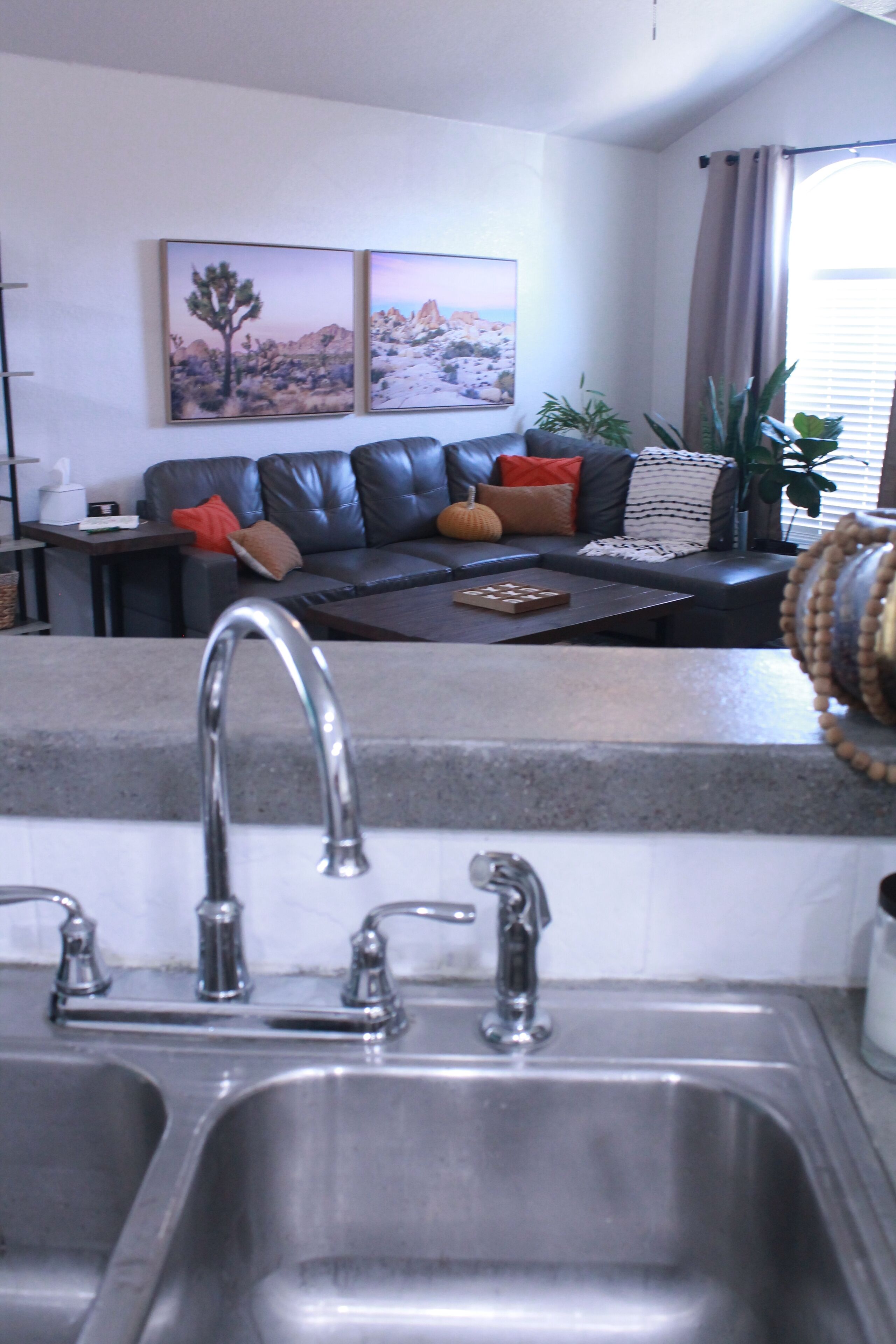 A kitchen with a double sink, a dining area with a black leather couch, and two paintings on the wall.