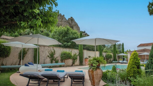 A poolside area with lounge chairs and umbrellas, a tiled deck, and a large planter with a plant.