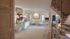 A spacious living area with a glass coffee table, a white armchair, and a beige carpet.