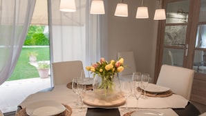 A dining table set with white plates, clear wine glasses, and a vase with yellow tulips.