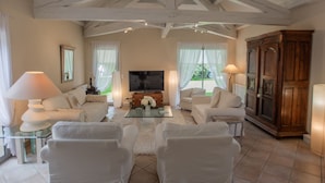 A spacious living room with a high ceiling, white furniture, a large flat-screen TV, and a wooden cabinet.
