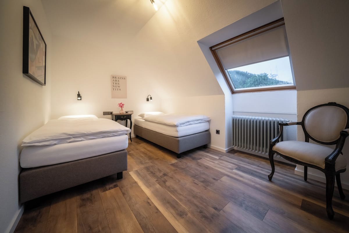 A bedroom with two beds, a chair, a window, and a radiator.