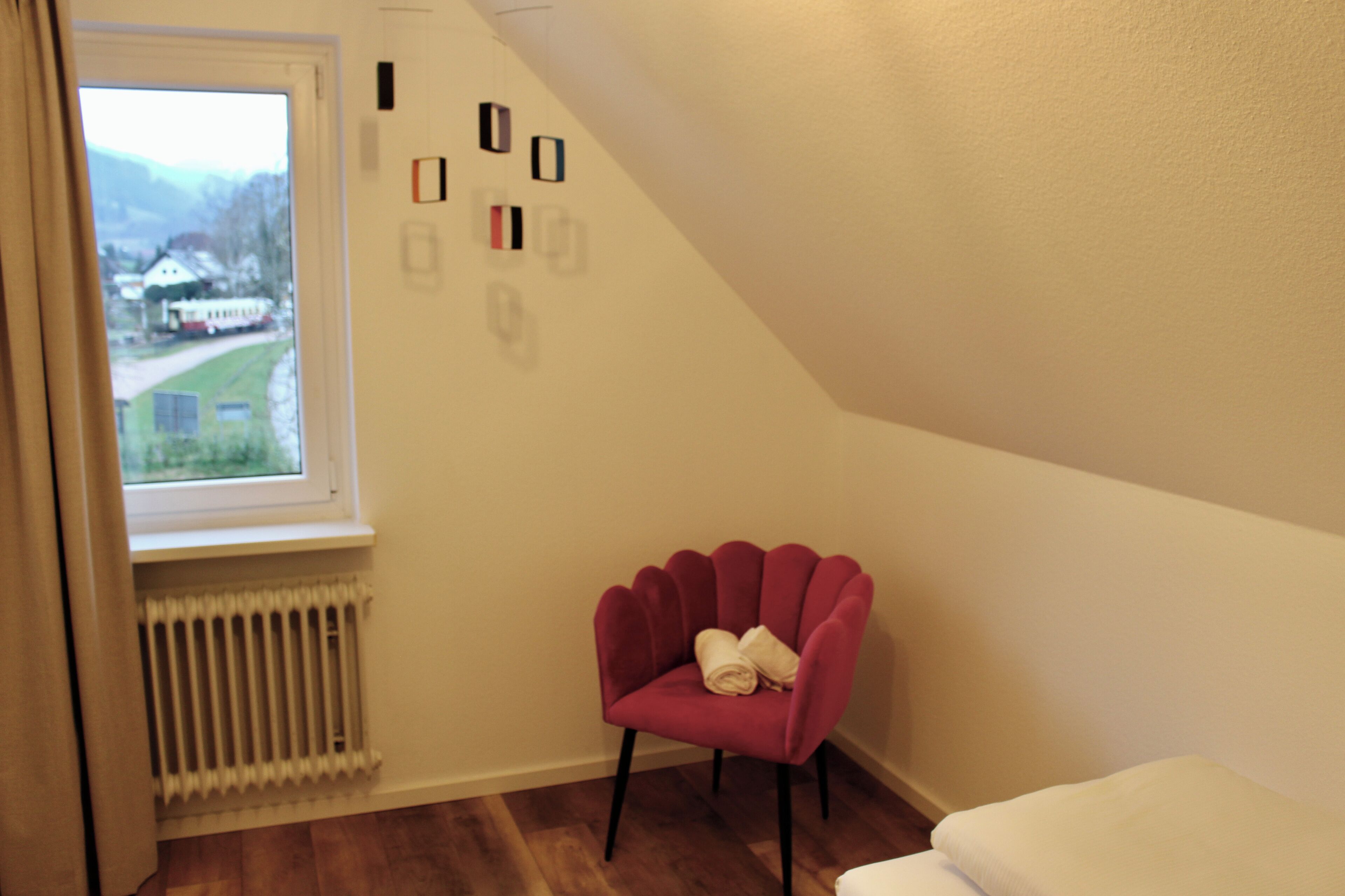 A room with a window, a radiator, a red chair, and a white bench.