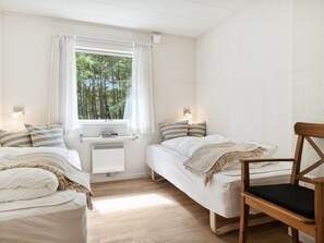 Una habitación pequeña y bien iluminada con dos camas individuales, una silla de madera y un ventanal con cortinas.