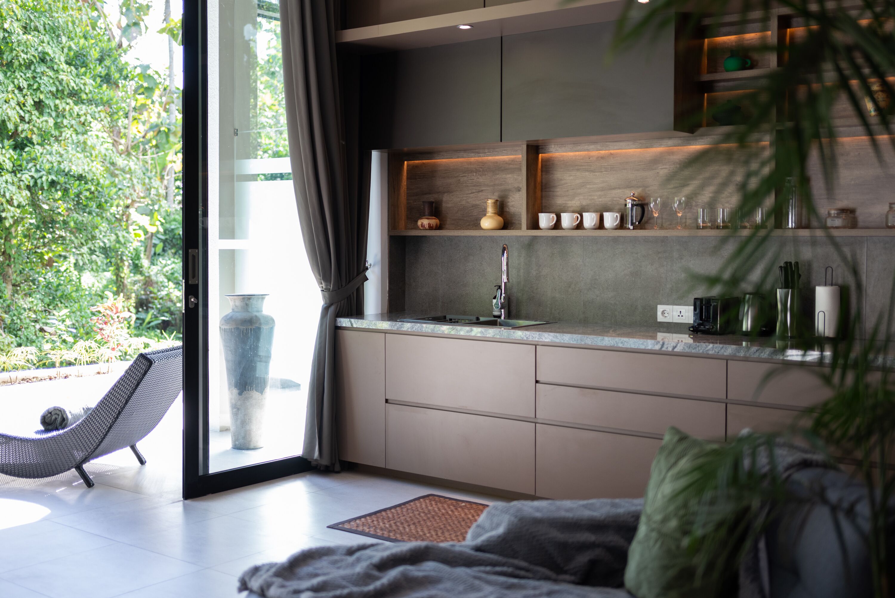 Una cocina moderna con un ventanal grande, estanterías empotradas y una zona de comedor con una silla acolchada.