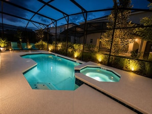 En swimmingpool med jacuzzi, omgivet af liggestole og planter, under et overdækket område.