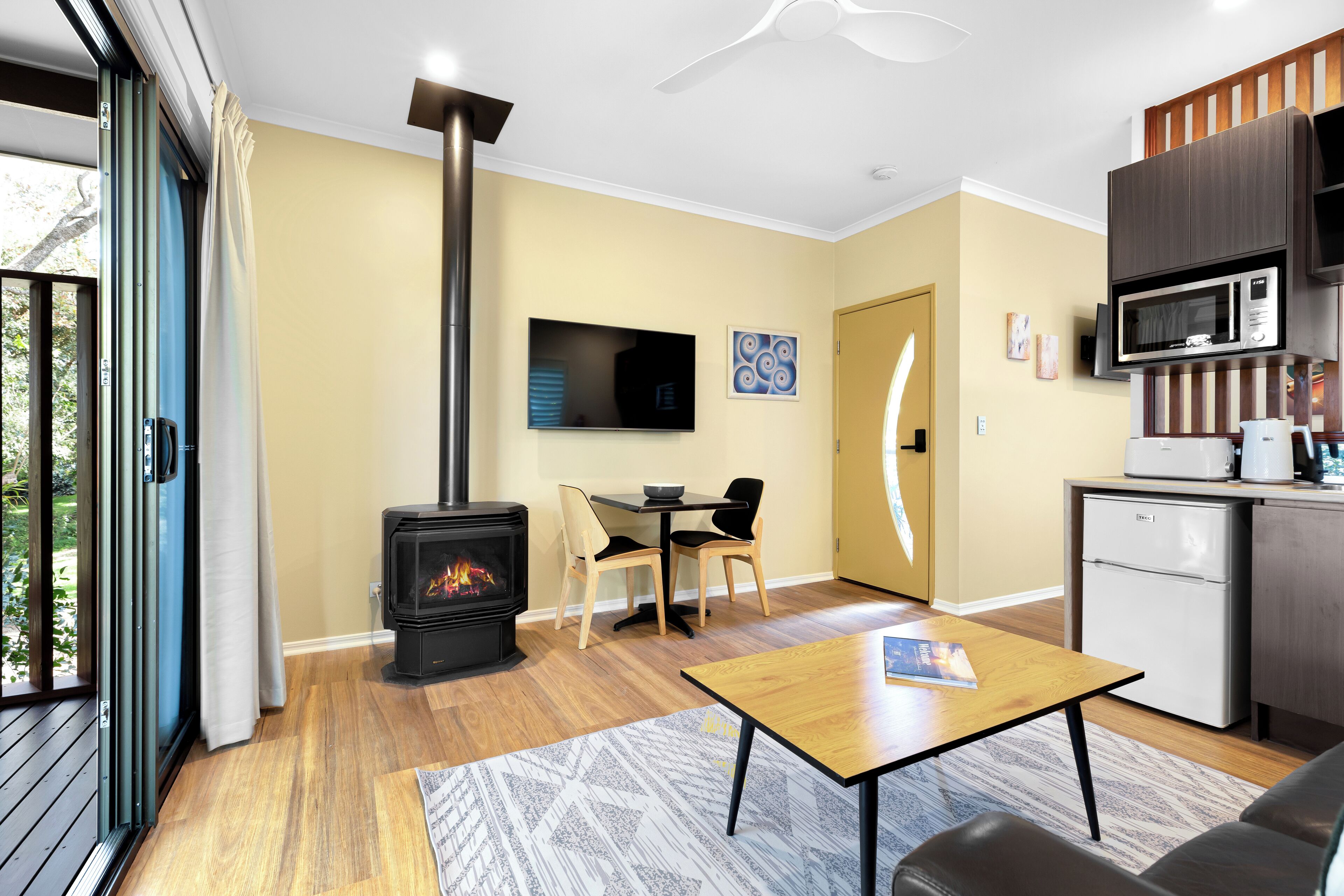 A modern living room with a wood-burning stove, a dining area, and a compact kitchen.