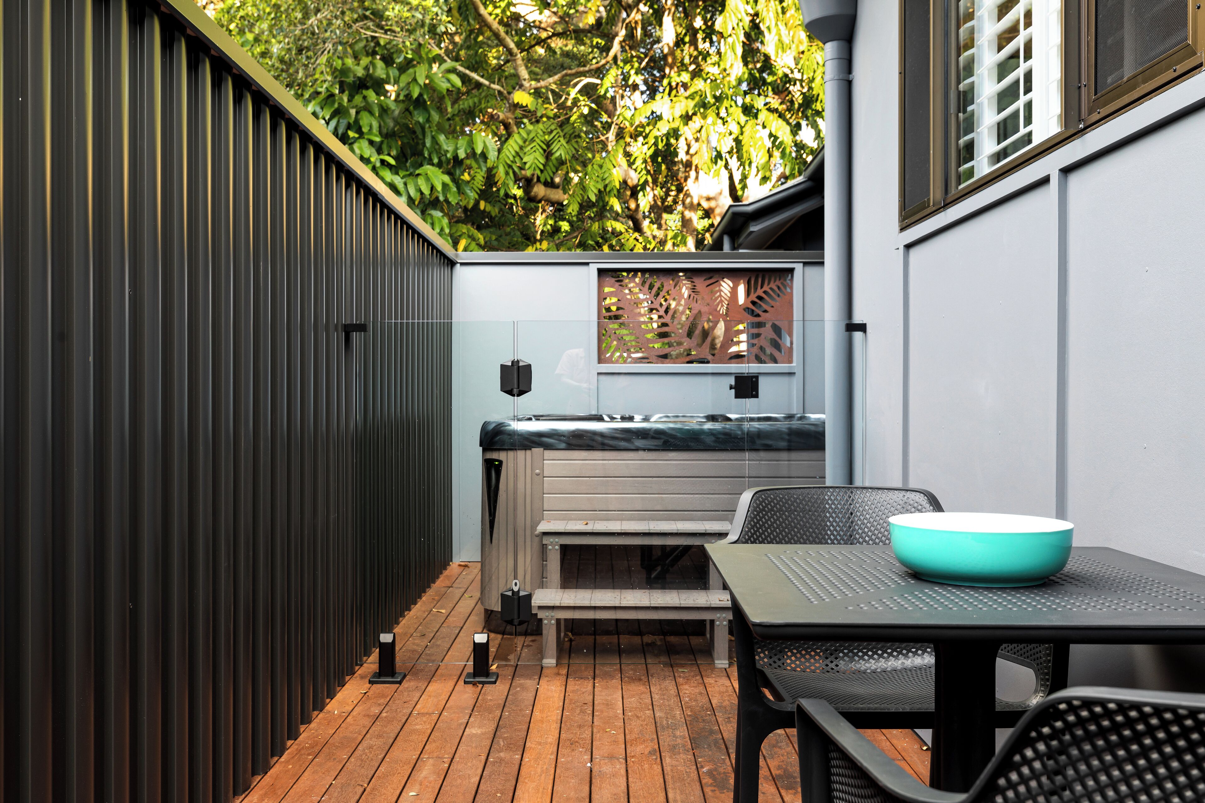 Eine Terrasse mit Holzboden, einer Bank, einem Tisch mit einer Schale und einem Metallzaun.