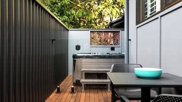 Eine Terrasse mit Holzboden, einer Bank, einem Tisch mit einer Schale und einem Metallzaun.