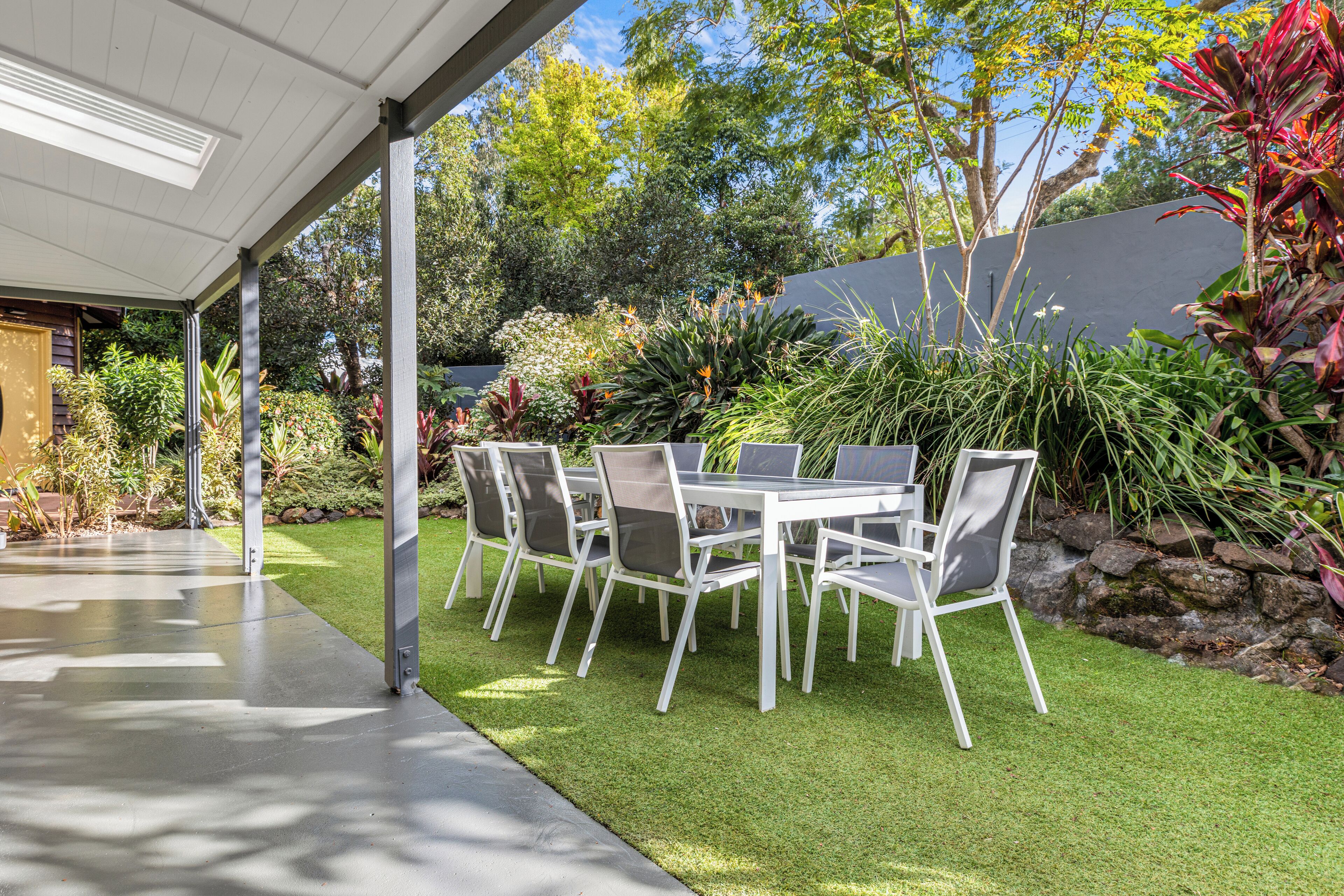 An outdoor patio with a table and chairs, surrounded by a well-maintained garden and a stone wall.