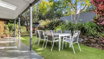 An outdoor patio with a table and chairs, surrounded by a well-maintained garden and a stone wall.