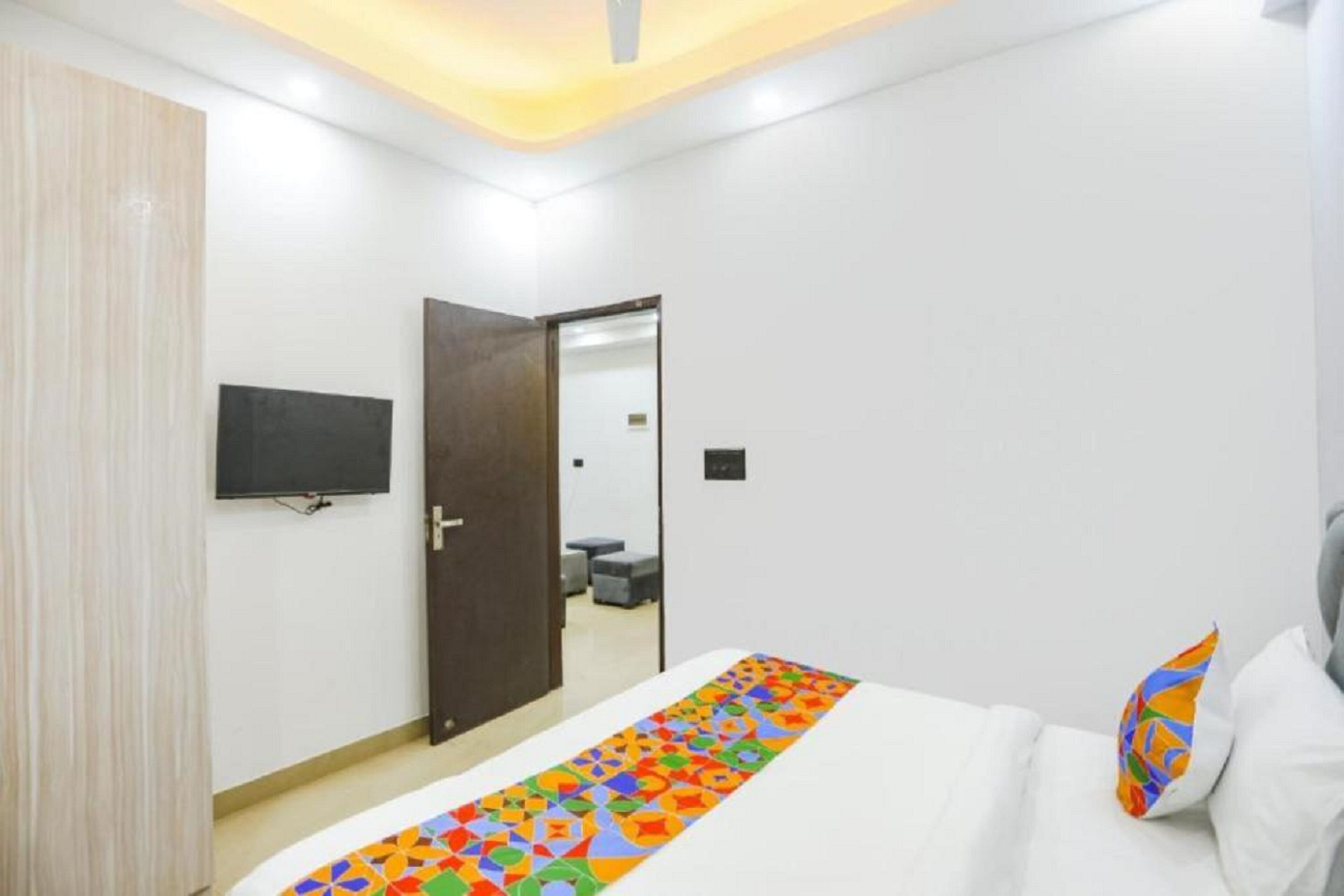 A modern hotel room with a bed, a TV mounted on the wall, and a door leading to a bathroom.
