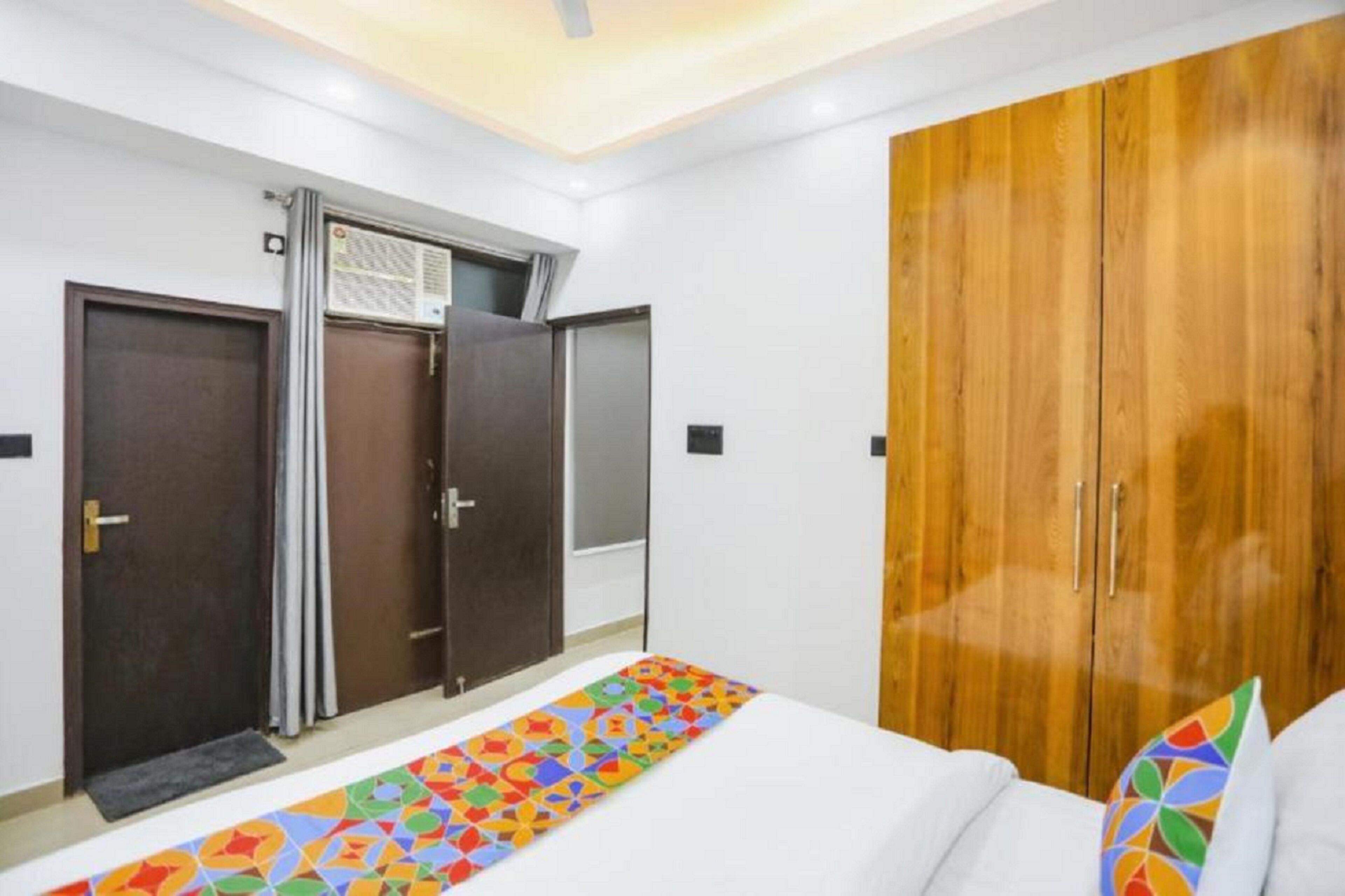 A bedroom with a bed, a wooden wardrobe, and a window with an air conditioning unit.