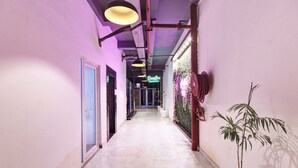 A hallway with a marble floor, a neon sign, and a potted plant. - Hotel The Rasa Kanti Nagar  (New Delhi)